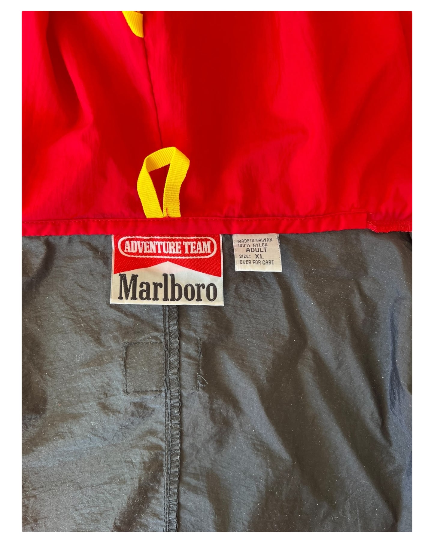 Vintage 1990s Marlboro Adventure Team Red and Black Nylon Windbreaker Jacket. Image depicts the brand and size tag.