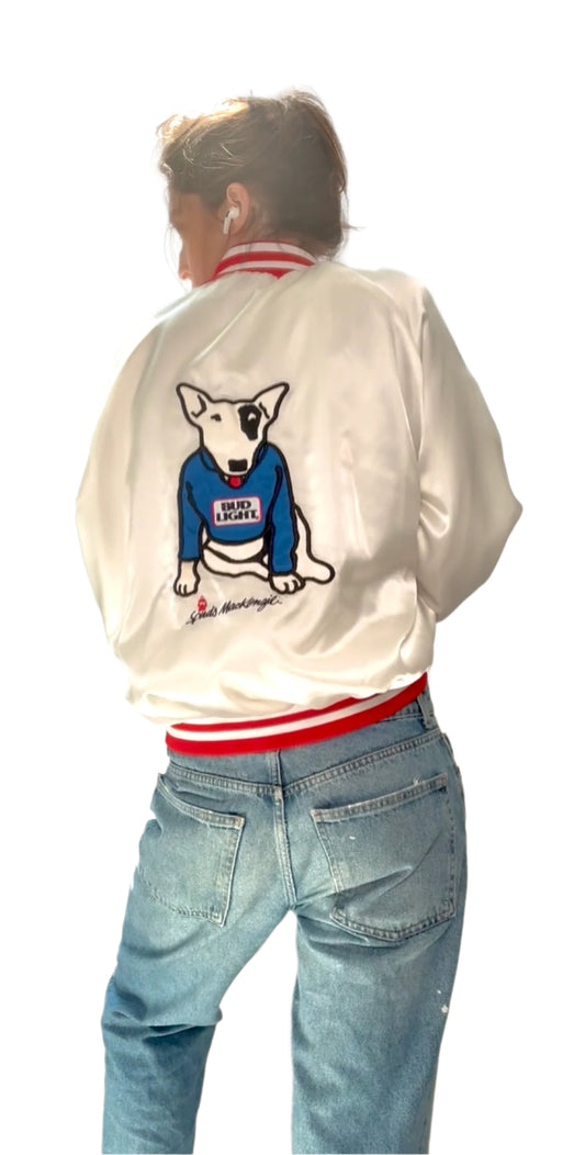 Person wearing a white jacket with a dog graphic and blue jeans against a white curtain background