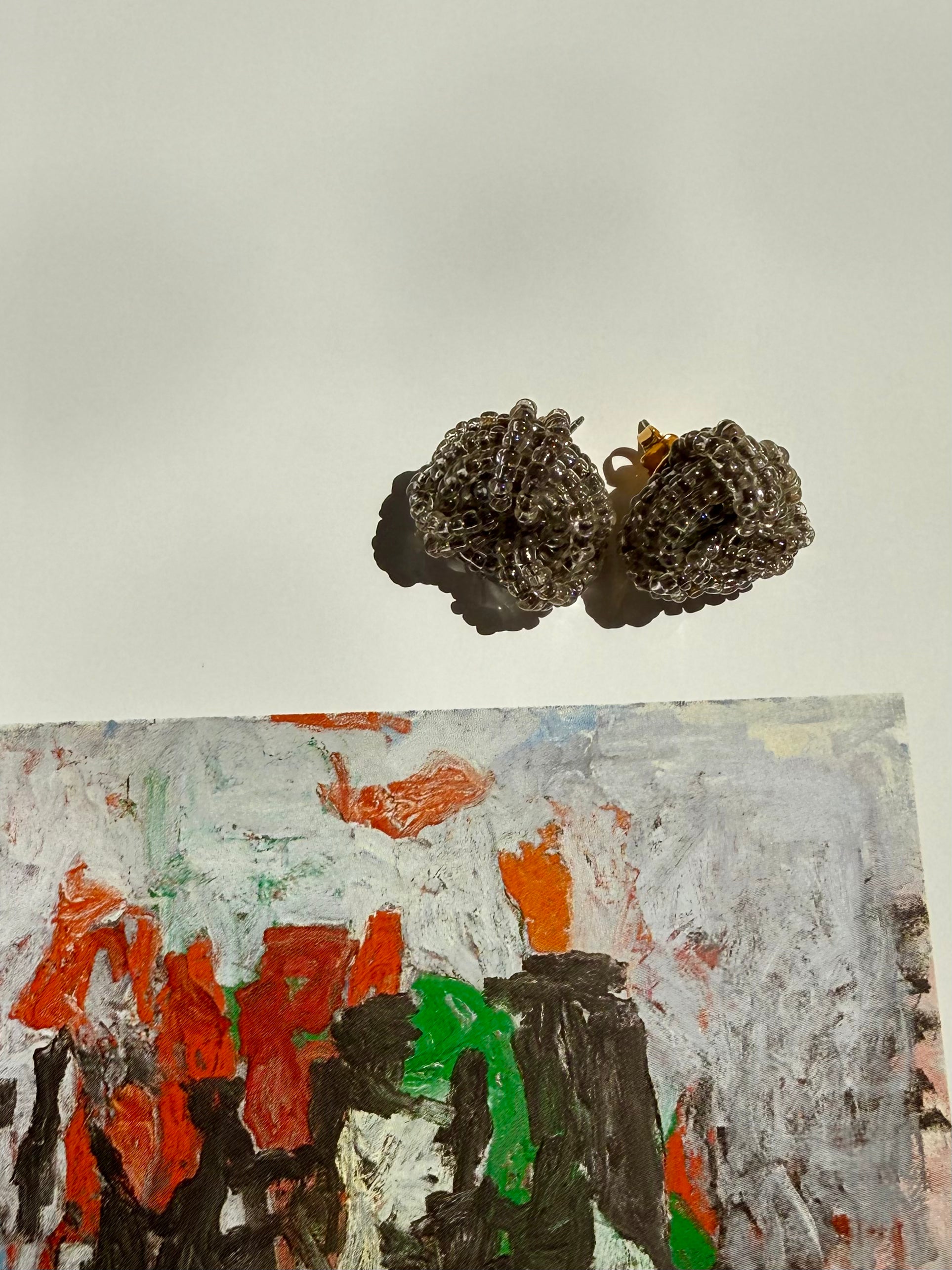 Pair of textured earrings above a colorful abstract painting on a light background