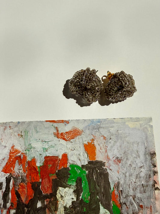 Pair of textured earrings above a colorful abstract painting on a light background