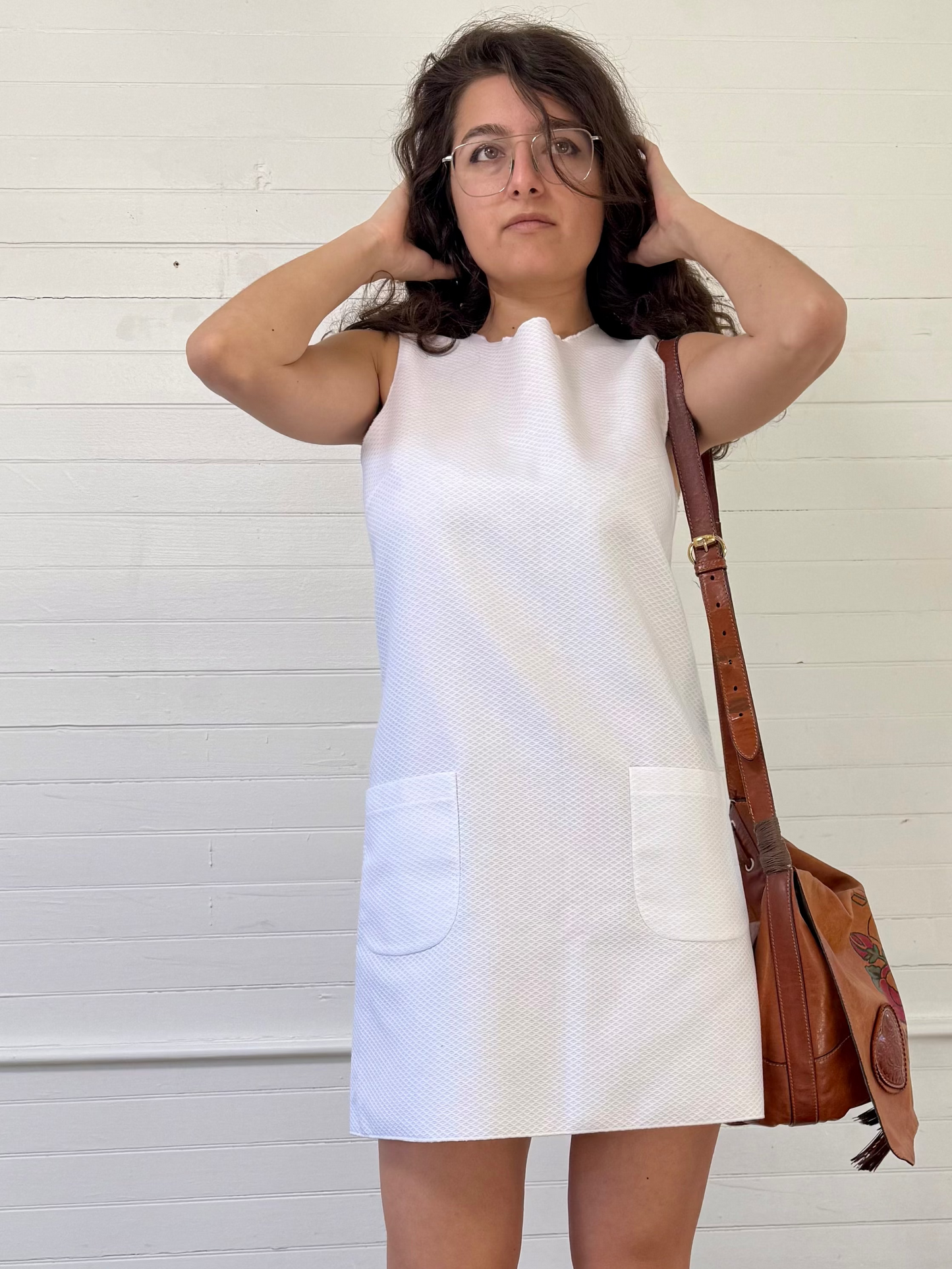 Woman in a white dress standing against a white wall with a red bucket on the floor.